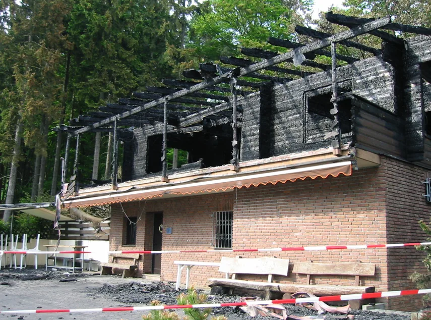 Das Clubhaus nach dem Brand: die obere Etage verkohlt, Absperrband davor.